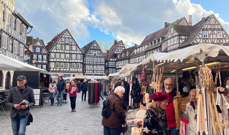 Ein belebter Krämermarkt in einer Altstadt mit Fachwerkhäusern. Menschen schlendern zwischen den Ständen unter einem blauen Himmel mit Wolken., © Stadt Schorndorf Ein belebter Krämermarkt in einer Altstadt mit Fachwerkhäusern. Menschen schlendern zwischen den Ständen unter einem blauen Himmel mit Wolken., © Stadt Schorndorf