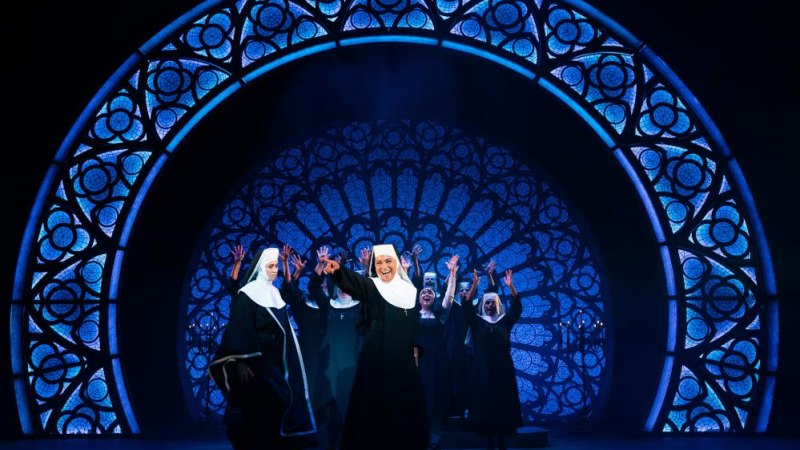 Nonnen tanzen auf der B&uuml;hne des Musicals Sister Act vor einem gro&szlig;en, leuchtenden Kirchenfenster. Die Szene ist lebhaft und farbenfroh., &copy; Ludwigsburg