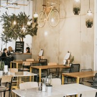 Modernes Caf&eacute; mit h&auml;ngendem Fahrrad an der Wand, Pflanzen und gem&uuml;tlichen Sitzbereichen. Menschen sitzen und unterhalten sich an Tischen., &copy; Claus Stuttgart