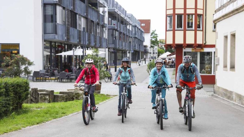 Vier Personen fahren mit Fahrrädern durch eine moderne Straße in Kirchheim unter Teck. Sie tragen Helme und Freizeitkleidung., © Schwäbische Alb Tourismusverband e.V.