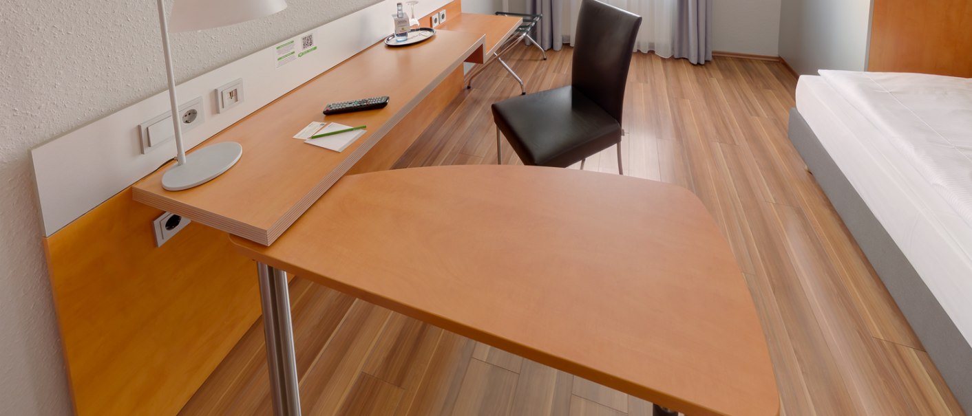 Modernes Einzelzimmer mit Holzfußboden, Schreibtisch, Stuhl, Flachbildfernseher und Bett. Helle Vorhänge und minimalistisches Design., © attimo Hotel Stuttgart