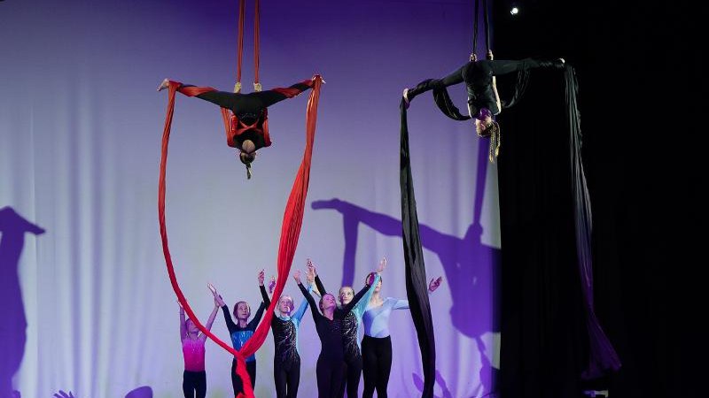 Kinder führen auf einer Bühne Luftakrobatik mit roten und schwarzen Tüchern vor, während andere Kinder im Hintergrund applaudieren., © Kunstschule Labyrinth Kinder führen auf einer Bühne Luftakrobatik mit roten und schwarzen Tüchern vor, während andere Kinder im Hintergrund applaudieren., © Kunstschule Labyrinth
