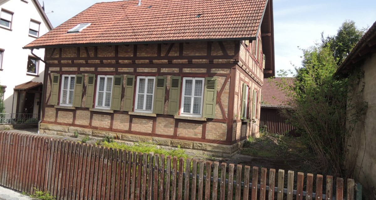 Fachwerkhaus mit roten Dachziegeln und grünen Fensterläden, umgeben von einem Holzzaun. Im Hintergrund sind weitere Gebäude sichtbar., © Land der 1000 Hügel - Kraichgau-Stromberg Fachwerkhaus mit roten Dachziegeln und grünen Fensterläden, umgeben von einem Holzzaun. Im Hintergrund sind weitere Gebäude sichtbar., © Land der 1000 Hügel - Kraichgau-Stromberg