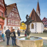 Eine Gruppe von Menschen betrachtet einen Brunnen auf einem historischen Platz in Plochingen. Fachwerkh&auml;user und eine Kirche im Hintergrund., &copy; PlochingenInfo