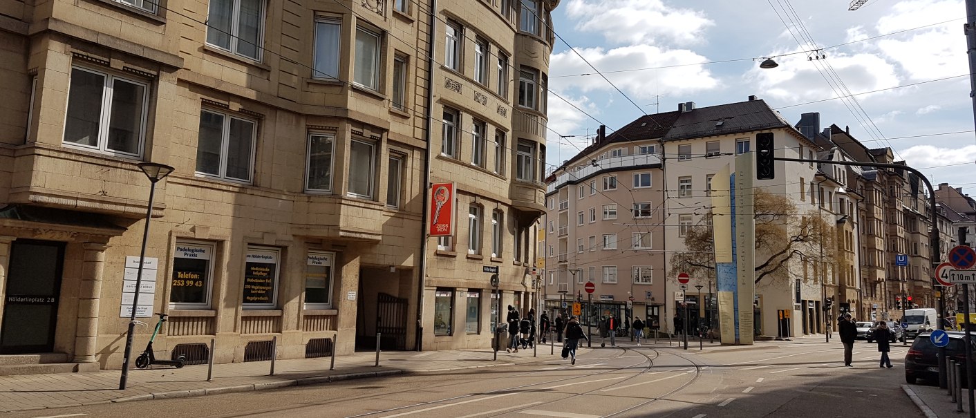 Städtische Straßenszene mit historischen Gebäuden, Straßenbahnschienen und Fußgängern. Ein E-Scooter steht an einem Laternenpfahl., © SMG