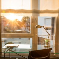 Ein moderner Schreibtisch mit Lampe steht vor einem Fenster. Die Sonne scheint herein und beleuchtet den Raum warm., © Hotel LOGIS Ein moderner Schreibtisch mit Lampe steht vor einem Fenster. Die Sonne scheint herein und beleuchtet den Raum warm., © Hotel LOGIS