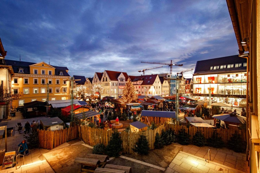 Abendlicher Weihnachtsmarkt in Göppingen mit festlich beleuchteten Ständen und einem großen Weihnachtsbaum, umgeben von historischen Gebäuden., © Stadt Göppingen