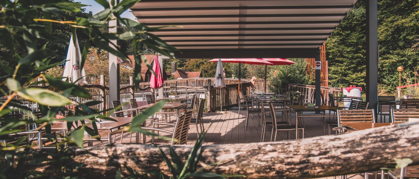Leere Terrasse mit Tischen und Stühlen unter einer Überdachung, umgeben von grünen Pflanzen und Sonnenschirmen., © Stadt Welzheim Leere Terrasse mit Tischen und Stühlen unter einer Überdachung, umgeben von grünen Pflanzen und Sonnenschirmen., © Stadt Welzheim