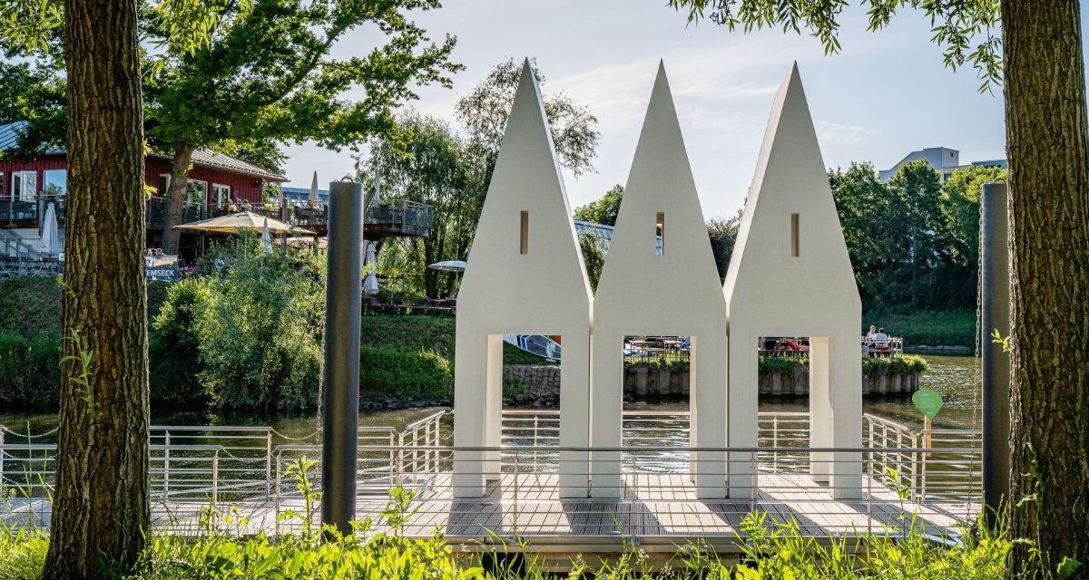 Drei wei&szlig;e, spitz zulaufende Strukturen stehen am Flussufer, umgeben von B&auml;umen. Im Hintergrund ist ein Geb&auml;ude mit Terrasse zu sehen., &copy; Remstal Tourismus e.V., , Architekt: Christoph M&auml;ckler Architekten, Frankfurt