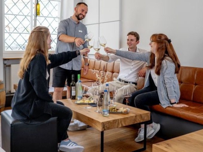 Vier Personen sitzen in einem modernen Raum und stoßen mit Weingläsern an. Auf dem Tisch stehen Weinflaschen und Snacks., © Esslinger Stadtmarketing & Tourismus GmbH Vier Personen sitzen in einem modernen Raum und stoßen mit Weingläsern an. Auf dem Tisch stehen Weinflaschen und Snacks., © Esslinger Stadtmarketing & Tourismus GmbH