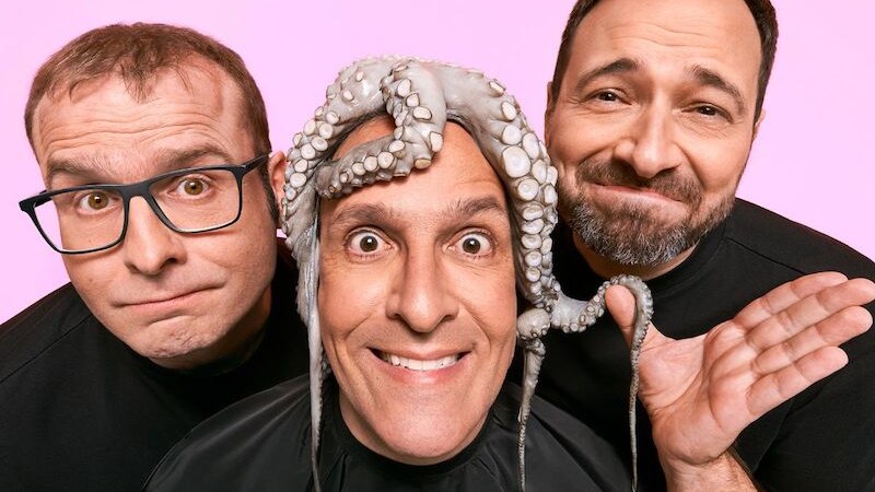 Drei M&auml;nner posieren humorvoll vor einem rosa Hintergrund. Einer tr&auml;gt einen Oktopus auf dem Kopf, w&auml;hrend die anderen zwei l&auml;cheln., &copy; Stadthalle Leonberg