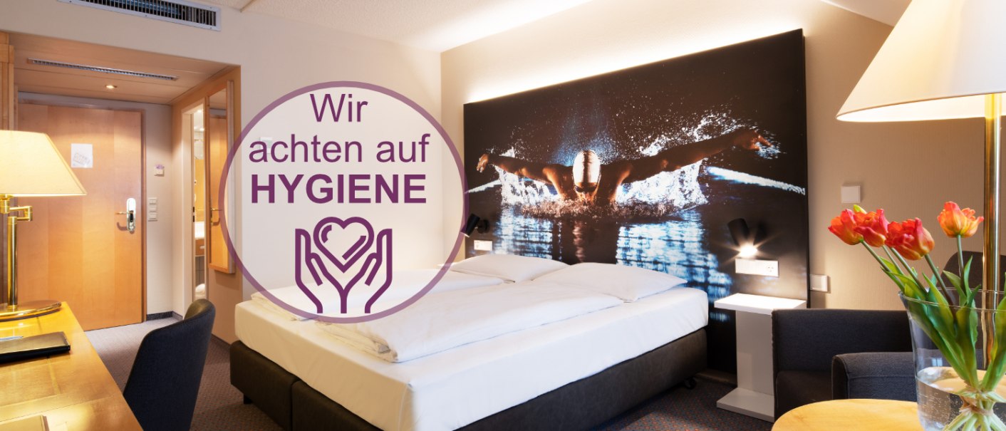 Modernes Hotelzimmer mit Doppelbett, großem Schwimmerbild an der Wand, Tisch mit Blumen und Hygienehinweis., © Erikson Hotel Modernes Hotelzimmer mit Doppelbett, großem Schwimmerbild an der Wand, Tisch mit Blumen und Hygienehinweis., © Erikson Hotel