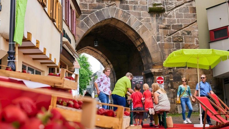 Menschen genie&szlig;en ein Erdbeerfest vor einem alten Torbogen. Im Vordergrund sind Erdbeeren in Kisten, im Hintergrund ein gr&uuml;ner Sonnenschirm., &copy; &copy;marketing-esslingen.de
