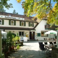 Ein Restaurant mit Terrasse, umgeben von Bäumen. Tische und Stühle stehen unter Sonnenschirmen. Das Gebäude hat grüne Fensterläden., © Kulinarium an der Glems