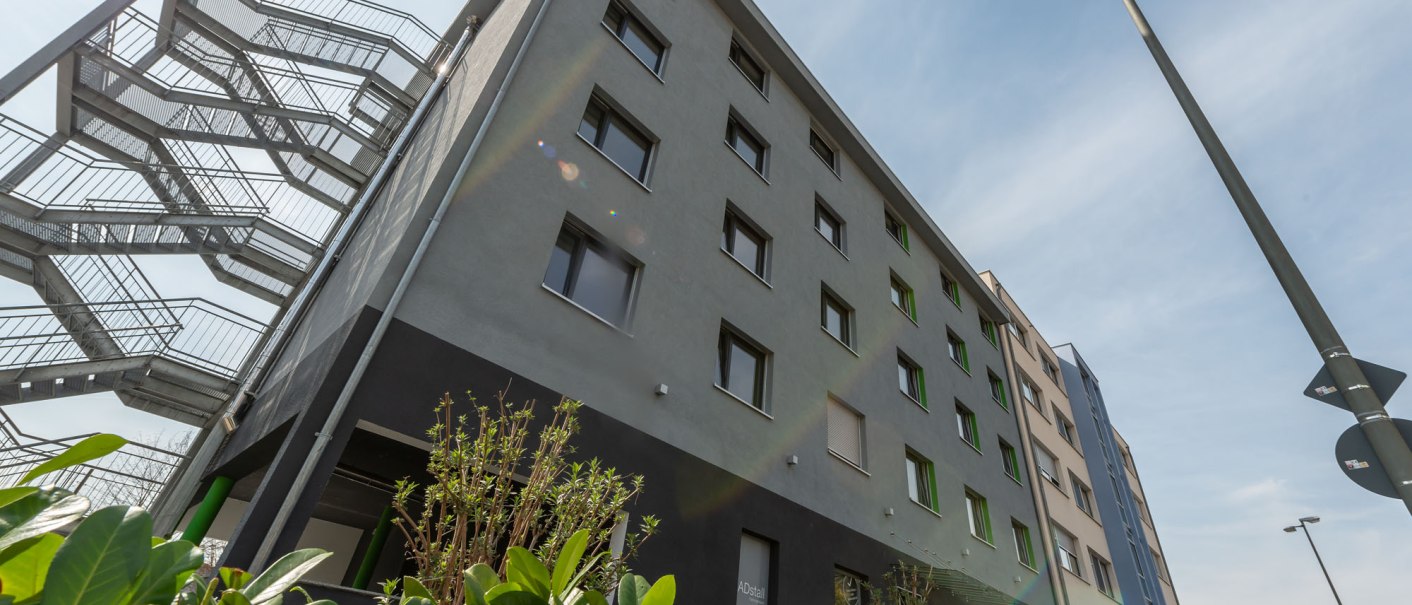Modernes Hotelgebäude mit Feuertreppe, umgeben von grünen Pflanzen, unter blauem Himmel., © a2 HOTELS Modernes Hotelgebäude mit Feuertreppe, umgeben von grünen Pflanzen, unter blauem Himmel., © a2 HOTELS