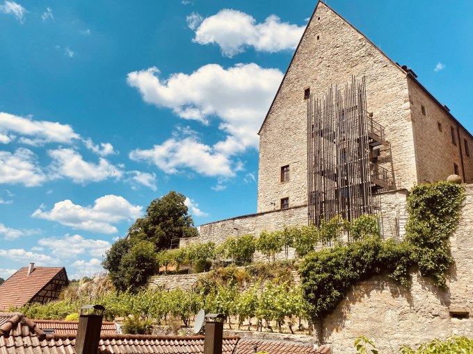 Ein historisches Gebäude mit Weinreben an einer Steinmauer unter einem klaren blauen Himmel mit weißen Wolken., © Stadt Besigheim Ein historisches Gebäude mit Weinreben an einer Steinmauer unter einem klaren blauen Himmel mit weißen Wolken., © Stadt Besigheim