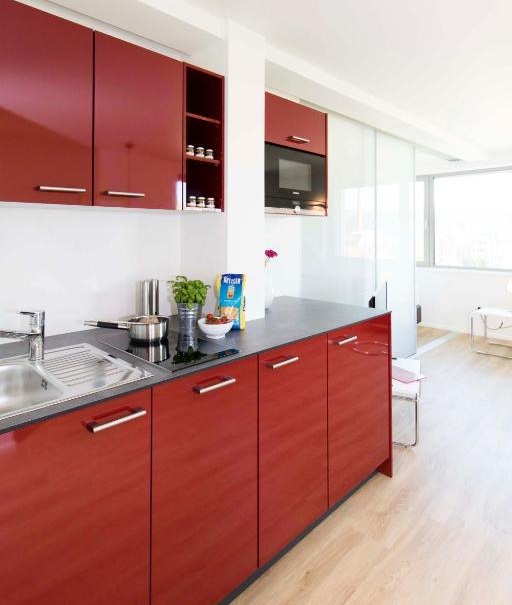 Moderne Küche mit roten Hochglanzschränken, Spüle, Herd und Holzfußboden. Helle, minimalistische Einrichtung mit viel Tageslicht., © Büroma-Apart Apartmentvermietung GmbH Moderne Küche mit roten Hochglanzschränken, Spüle, Herd und Holzfußboden. Helle, minimalistische Einrichtung mit viel Tageslicht., © Büroma-Apart Apartmentvermietung GmbH