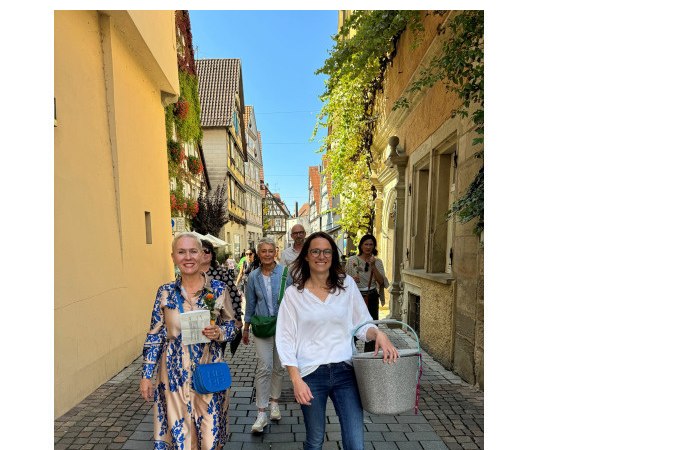 Eine Gruppe von Menschen spaziert fr&ouml;hlich durch eine malerische Altstadtstra&szlig;e mit Fachwerkh&auml;usern und Pflanzen an den W&auml;nden., &copy; Eigenbetrieb Tourismus und Citymanagement Schorndorf