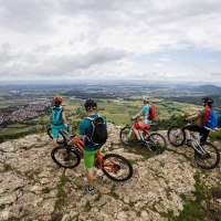 Vier Mountainbiker stehen auf einem Felsen und blicken auf eine weite Landschaft mit Feldern und Dörfern. Der Himmel ist bewölkt., © Schwäbische Alb Tourismusverband e.V.