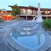 Moderner Brunnen mit geschwungenen Formen und Wasserbecken vor einem beleuchteten Gebäude mit Terrasse und Pflanzen., © Waiblingen - Stuttgart-Marketing GmbH Moderner Brunnen mit geschwungenen Formen und Wasserbecken vor einem beleuchteten Gebäude mit Terrasse und Pflanzen., © Waiblingen - Stuttgart-Marketing GmbH