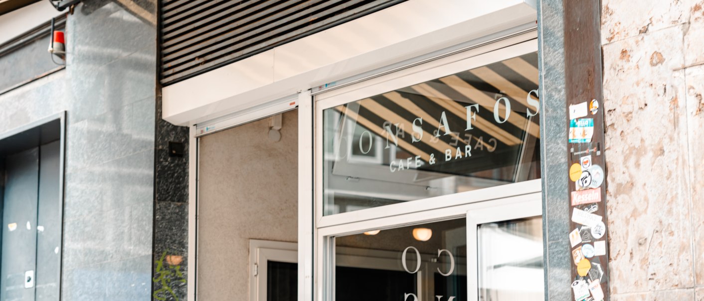 Eingang eines Cafés mit der Aufschrift 'ConSafos Café & Bar' auf der Glastür. Daneben eine Wand mit Aufklebern., © SMG Stuttgart Marketing GmbH - Sarah Schmid