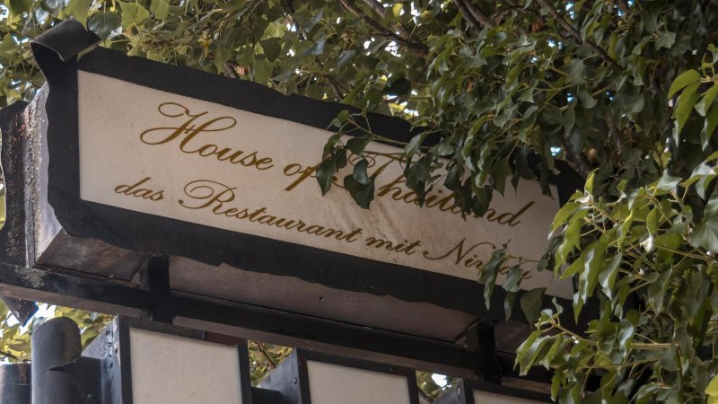 Ein Schild mit der Aufschrift 'House of Thailand, das Restaurant mit Niveau', umgeben von grünen Blättern., © Stuttgart Marketing GmbH, Sarah Schmid Ein Schild mit der Aufschrift 'House of Thailand, das Restaurant mit Niveau', umgeben von grünen Blättern., © Stuttgart Marketing GmbH, Sarah Schmid