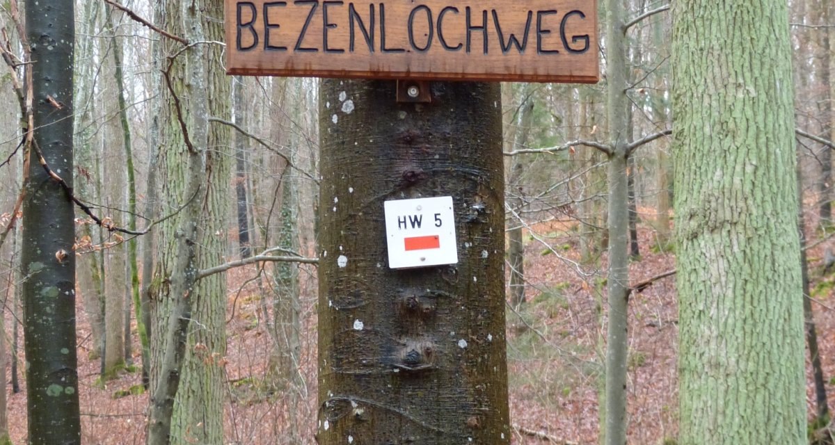 Ein Holzschild mit der Aufschrift 'BEZENLOCHWEG' hängt an einem Baum im Wald. Darunter befinden sich zwei Wandermarkierungen., © Natur.Nah. Schönbuch & Heckengäu Ein Holzschild mit der Aufschrift 'BEZENLOCHWEG' hängt an einem Baum im Wald. Darunter befinden sich zwei Wandermarkierungen., © Natur.Nah. Schönbuch & Heckengäu