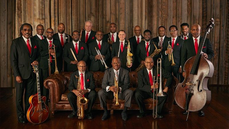 Eine Jazzband in Anzügen mit roten Krawatten posiert mit Instrumenten vor einer Holzwand., © Backnang Eine Jazzband in Anzügen mit roten Krawatten posiert mit Instrumenten vor einer Holzwand., © Backnang