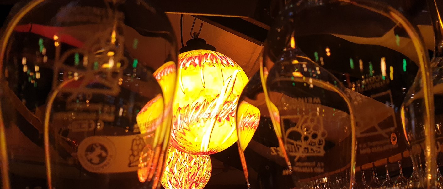 Weingläser reflektieren eine gelb-rote Lampe, die warmes Licht ausstrahlt. Die Szene wirkt gemütlich und einladend., © Weingut Ruoff Weingläser reflektieren eine gelb-rote Lampe, die warmes Licht ausstrahlt. Die Szene wirkt gemütlich und einladend., © Weingut Ruoff