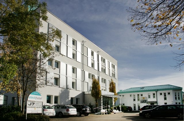 Modernes Hotelgebäude mit mehreren Stockwerken, umgeben von Bäumen. Autos parken vor dem Eingang. Schild mit Hotelnamen sichtbar., © ateckhotel Modernes Hotelgebäude mit mehreren Stockwerken, umgeben von Bäumen. Autos parken vor dem Eingang. Schild mit Hotelnamen sichtbar., © ateckhotel