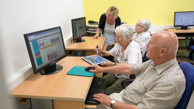 Senioren sitzen an Computern in einem Schulungsraum. Eine Frau steht und erklärt etwas. Alle wirken konzentriert und interessiert., © ©Roberto Bulgrin