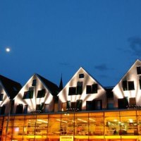 Ein modernes Gebäude mit beleuchteten Giebeln und Glasfassade bei Nacht. Der Mond ist am klaren Himmel sichtbar., © Hotel an der Stadtmauer