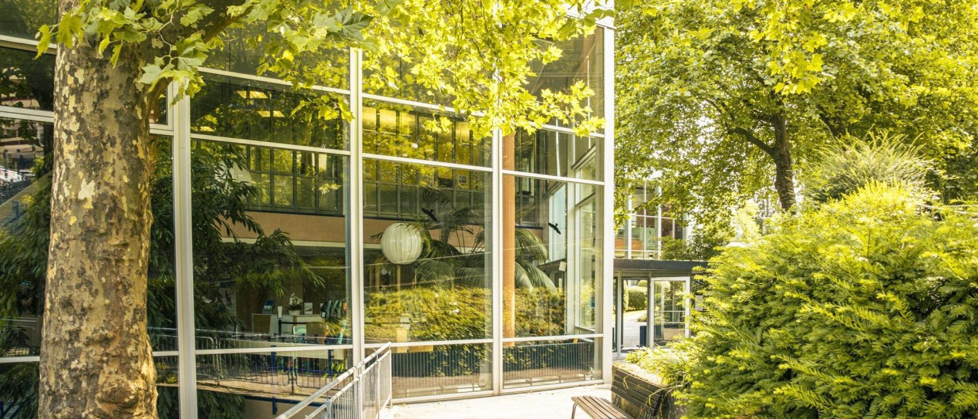 Moderne Glasfassade eines Gebäudes, umgeben von üppigem Grün und Bäumen, die sich im Glas spiegeln., © Stuttgart-Marketing GmbH, Sarah Schmid Moderne Glasfassade eines Gebäudes, umgeben von üppigem Grün und Bäumen, die sich im Glas spiegeln., © Stuttgart-Marketing GmbH, Sarah Schmid