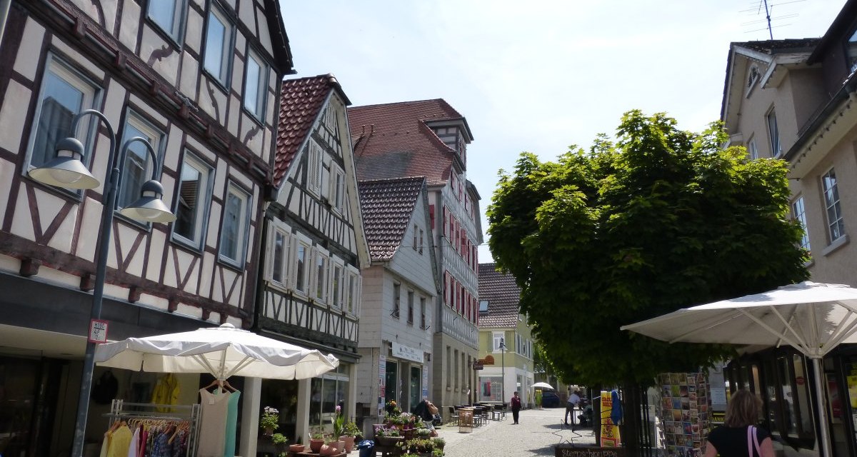 Fußgängerzone in Vaihingen an der Enz mit Fachwerkhäusern, Geschäften und Passanten. Sonnenschirme und ein Baum spenden Schatten., © Land der 1000 Hügel - Kraichgau-Stromberg Fußgängerzone in Vaihingen an der Enz mit Fachwerkhäusern, Geschäften und Passanten. Sonnenschirme und ein Baum spenden Schatten., © Land der 1000 Hügel - Kraichgau-Stromberg
