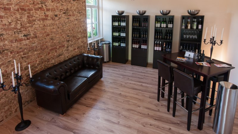Gemütliche Vinothek mit Ledersofa, Weinregalen und Stehtisch. Ziegelwand und Kerzenständer verleihen dem Raum eine elegante Atmosphäre., © Weingut Zaißerei Gemütliche Vinothek mit Ledersofa, Weinregalen und Stehtisch. Ziegelwand und Kerzenständer verleihen dem Raum eine elegante Atmosphäre., © Weingut Zaißerei