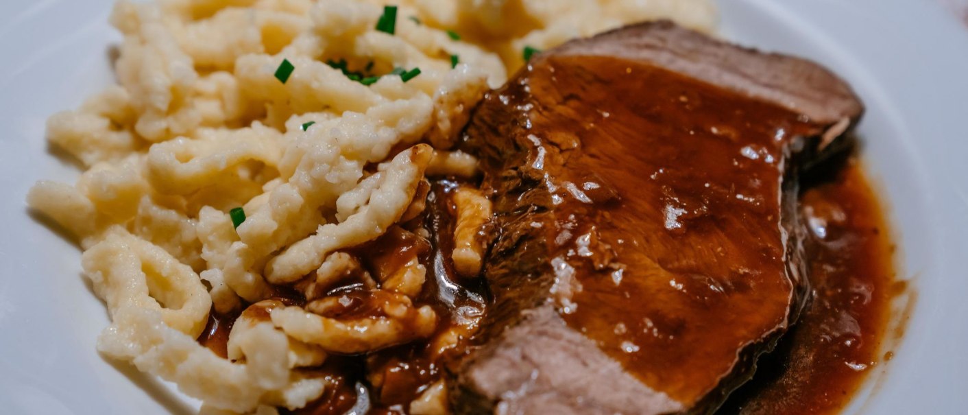 Ein Teller mit saftigem Braten in dunkler Soße, serviert mit Spätzle, garniert mit Schnittlauch., © SMG, Thomas Niedermüller Ein Teller mit saftigem Braten in dunkler Soße, serviert mit Spätzle, garniert mit Schnittlauch., © SMG, Thomas Niedermüller