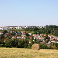 Ein Heuballen auf einem Feld mit Blick auf ein Wohngebiet mit roten Dächern und grünen Bäumen im Hintergrund., © Natur.Nah. Schönbuch & Heckengäu Ein Heuballen auf einem Feld mit Blick auf ein Wohngebiet mit roten Dächern und grünen Bäumen im Hintergrund., © Natur.Nah. Schönbuch & Heckengäu