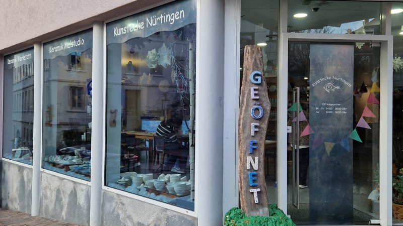 Au&szlig;enansicht eines Keramikstudios mit gro&szlig;en Fenstern. Ein Schild mit 'Ge&ouml;ffnet' steht vor der T&uuml;r. Innen sind Keramiken und Dekorationen sichtbar., &copy; StadtN&uuml;rtingen