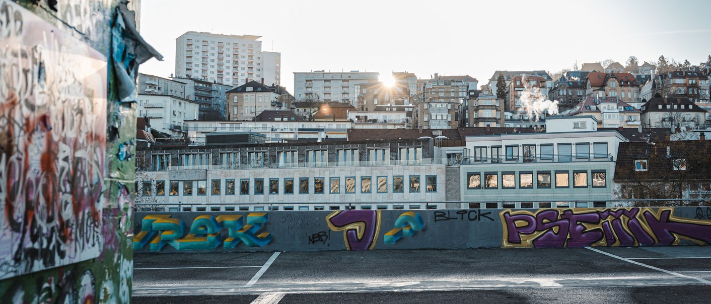 Städtische Skyline von Stuttgart bei Sonnenuntergang, mit Graffiti auf einer Mauer im Vordergrund. Gebäude und Rauch steigen in den Himmel., © SMG Stuttgart Marketing GmbH -Sarah Schmid Städtische Skyline von Stuttgart bei Sonnenuntergang, mit Graffiti auf einer Mauer im Vordergrund. Gebäude und Rauch steigen in den Himmel., © SMG Stuttgart Marketing GmbH -Sarah Schmid