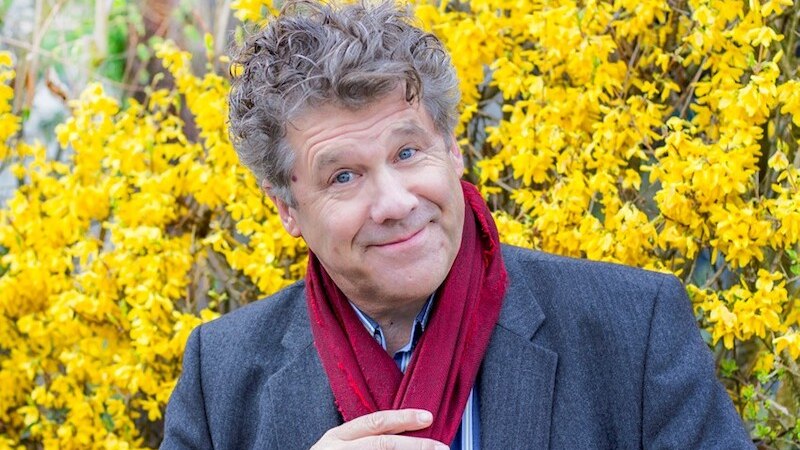 Ein Mann mit lockigem Haar und rotem Schal l&auml;chelt vor einem Hintergrund aus gelben Blumen., &copy; Stadt Leinfelden-Echterdingen, Kulturamt