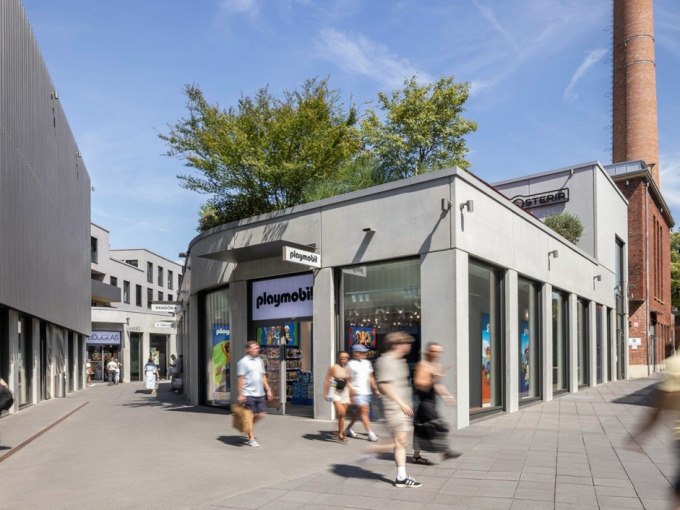 Menschen gehen an einem Playmobil-Gesch&auml;ft in der Outletcity Metzingen vorbei. Moderne Architektur und ein Schornstein im Hintergrund., &copy; Schlienz-Tours GmbH &amp; Co.KG