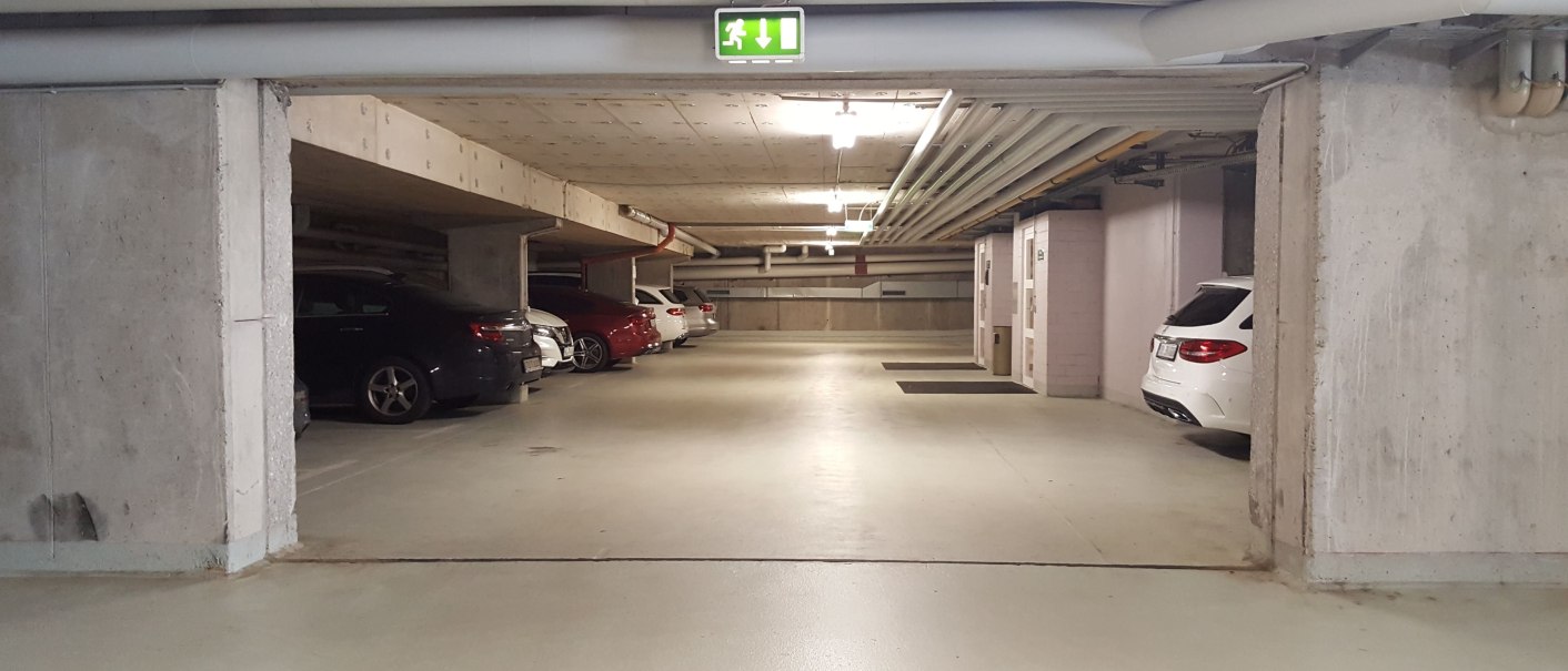 Unterirdischer Parkplatz mit geparkten Autos und einem Notausgangsschild an der Decke., © Erikson Hotel Unterirdischer Parkplatz mit geparkten Autos und einem Notausgangsschild an der Decke., © Erikson Hotel