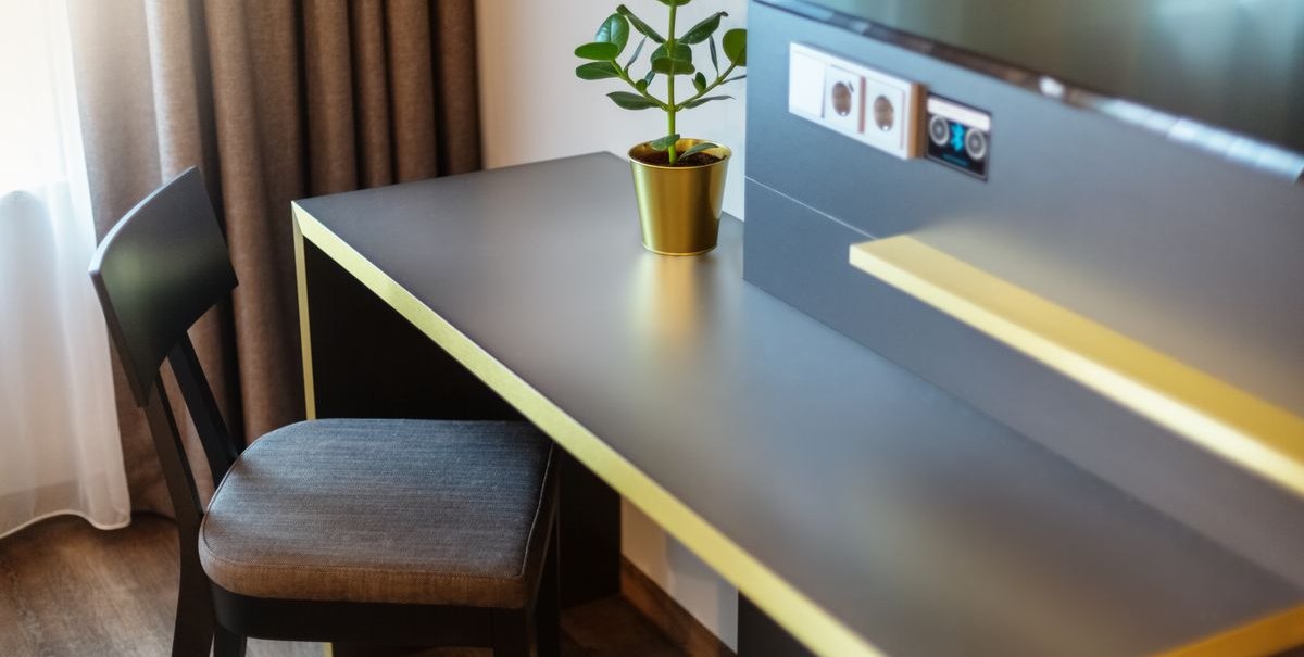 Moderner Schreibtisch mit gelben Akzenten, Topfpflanze und Stuhl vor einem Fenster mit Vorhängen. Steckdosen und Bluetooth-Anschluss an der Wand., © Novum Hospitality Moderner Schreibtisch mit gelben Akzenten, Topfpflanze und Stuhl vor einem Fenster mit Vorhängen. Steckdosen und Bluetooth-Anschluss an der Wand., © Novum Hospitality