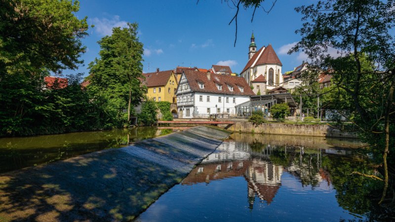 Die Rems in Waiblingen mit Fachwerkh&auml;usern und einer Kirche im Hintergrund, umgeben von B&auml;umen und blauem Himmel., &copy; Remstal Tourismus e.V.