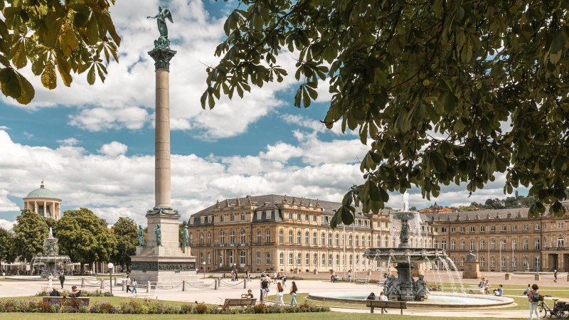 Der Schlossplatz in Stuttgart zeigt die Jubiläumssäule und das Neue Schloss. Menschen genießen den sonnigen Tag, während Bäume den Platz säumen., © SMG, Sarah Schmid Der Schlossplatz in Stuttgart zeigt die Jubiläumssäule und das Neue Schloss. Menschen genießen den sonnigen Tag, während Bäume den Platz säumen., © SMG, Sarah Schmid