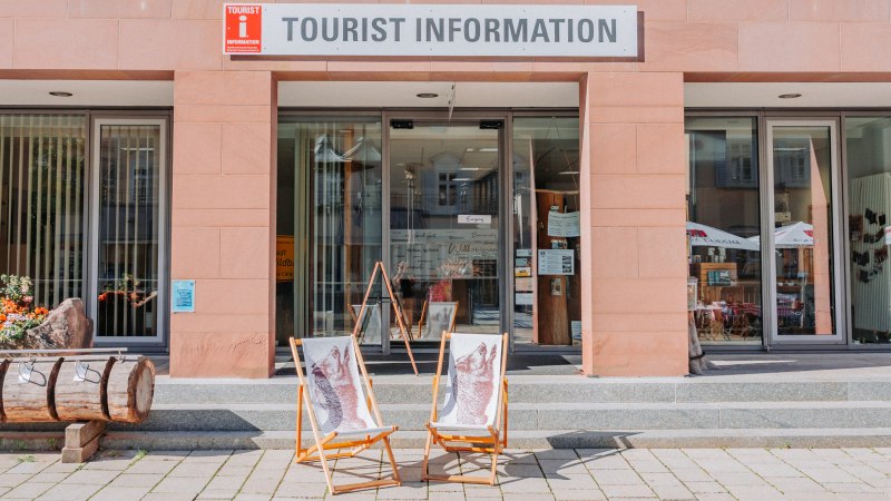 Die TOURIST INFORMATION mit Glasfront und zwei Liegestühlen vor dem Eingang. Vor dem Gebäude stehen Blumen und ein Holzstamm., © Touristik Bad Wildbad GmbH Die TOURIST INFORMATION mit Glasfront und zwei Liegestühlen vor dem Eingang. Vor dem Gebäude stehen Blumen und ein Holzstamm., © Touristik Bad Wildbad GmbH