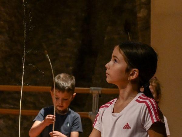 Kinder balancieren Federn auf den Fingern in einem Workshop. Ein Mädchen im Vordergrund konzentriert sich, während ein Junge im Hintergrund ebenfalls übt., © Kunstschule Labyrinth