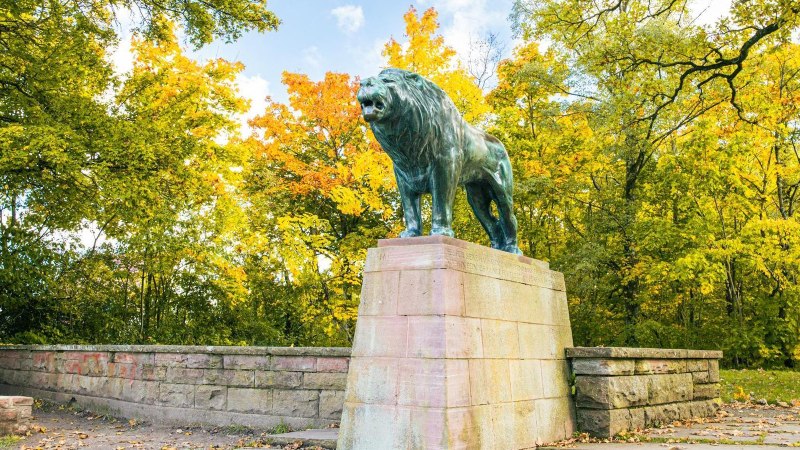 Eine imposante L&ouml;wenstatue steht auf einem Sockel, umgeben von herbstlich gef&auml;rbten B&auml;umen in einem Park., &copy; Stuttgart-Marketing GmbH, Sarah Schmid