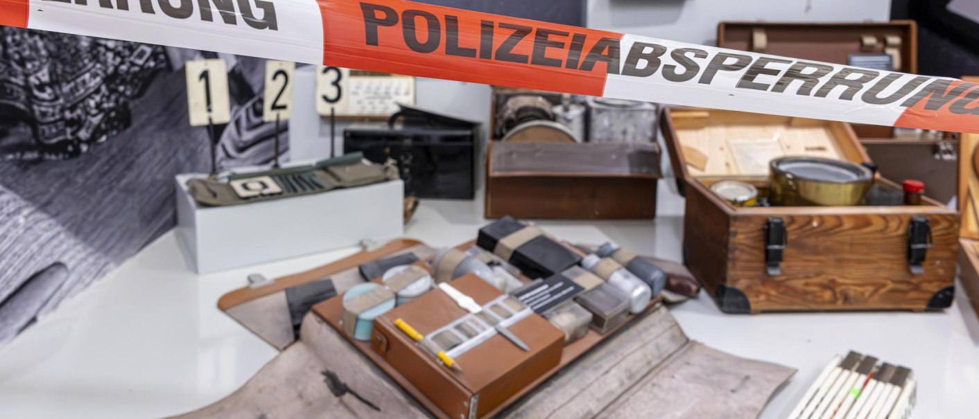 Ausstellungsstücke im Polizeimuseum Stuttgart, darunter alte Polizeiausrüstung und Beweismaterial, hinter einem Absperrband mit der Aufschrift 'POLIZEIABSPERRUNG'., © Stuttgart-Marketing GmbH, Sarah Schmid