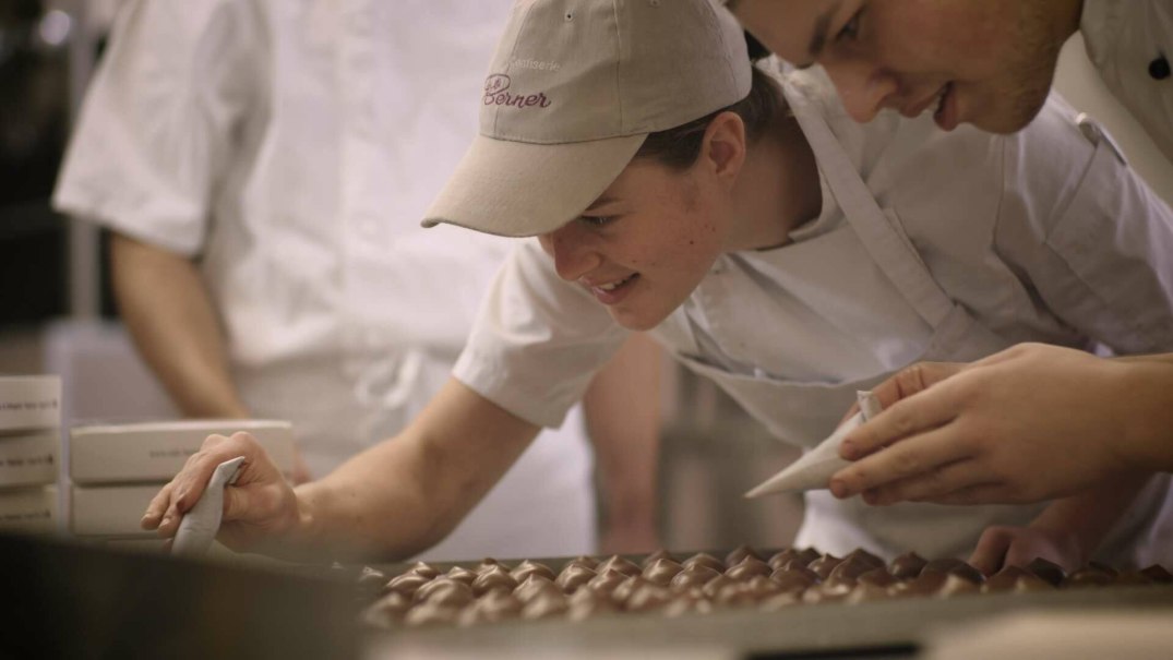 Zwei Personen in weißen Schürzen dekorieren Pralinen in einer Konditorei. Sie konzentrieren sich auf die Details der Schokoladenkreationen. Zwei Personen in weißen Schürzen dekorieren Pralinen in einer Konditorei. Sie konzentrieren sich auf die Details der Schokoladenkreationen.